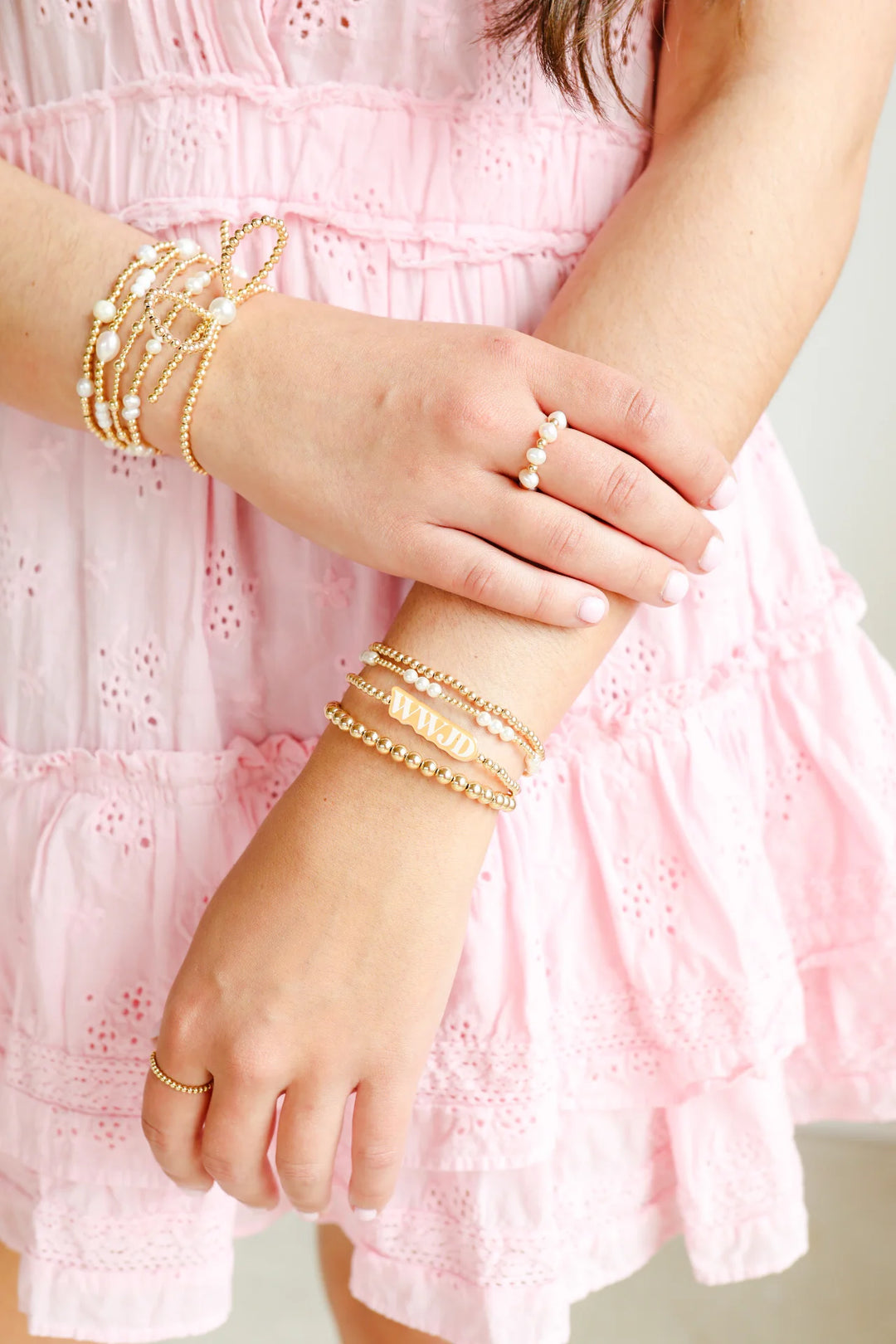 Close-up of a person wearing gold bracelets and a ring on a pink dress.