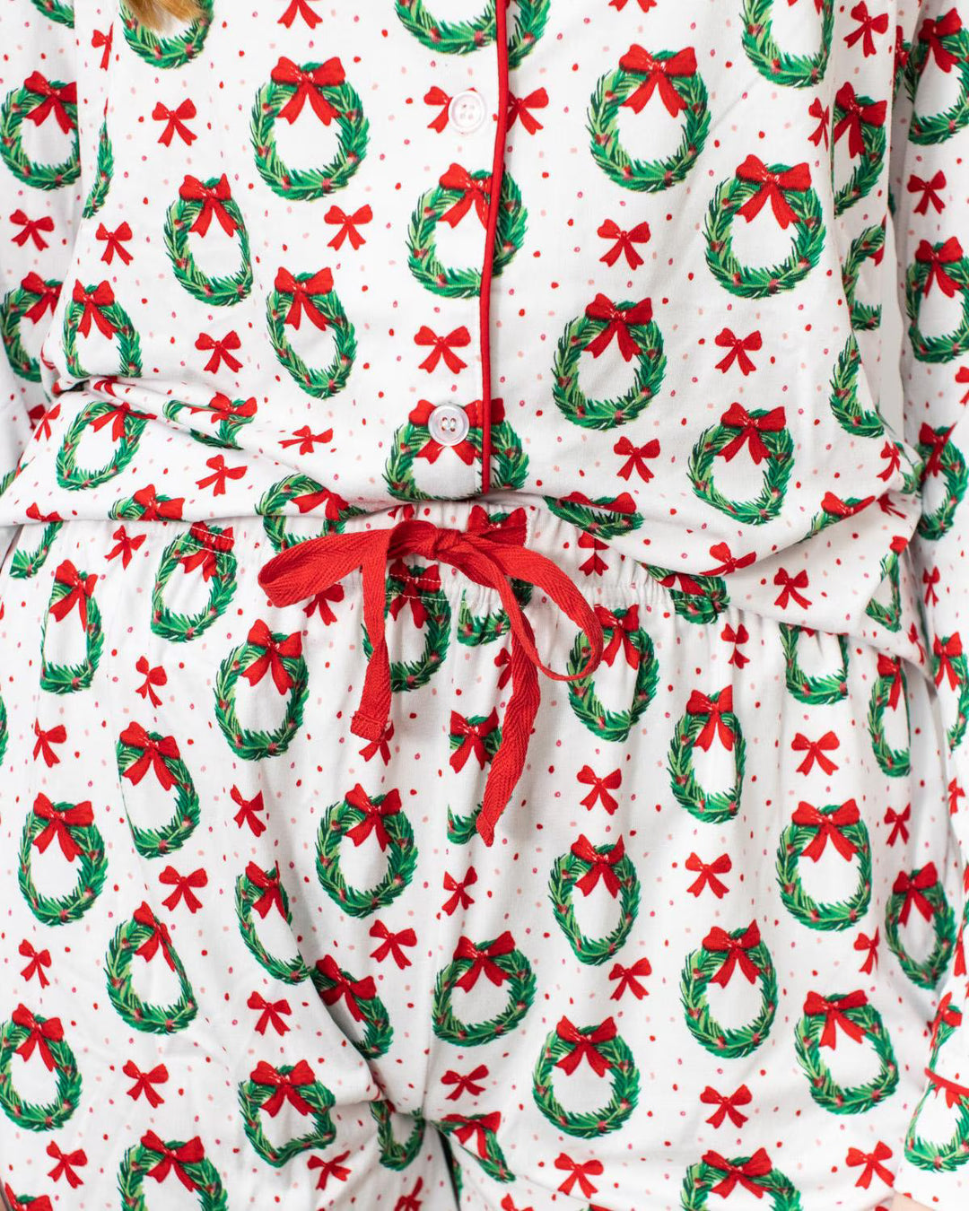 Close up of Christmas-themed pajama bottoms with wreath and bow pattern and drawstring waistband