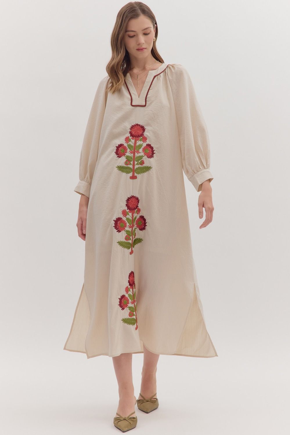 Woman wearing a beige dress with floral embroidery on a white background