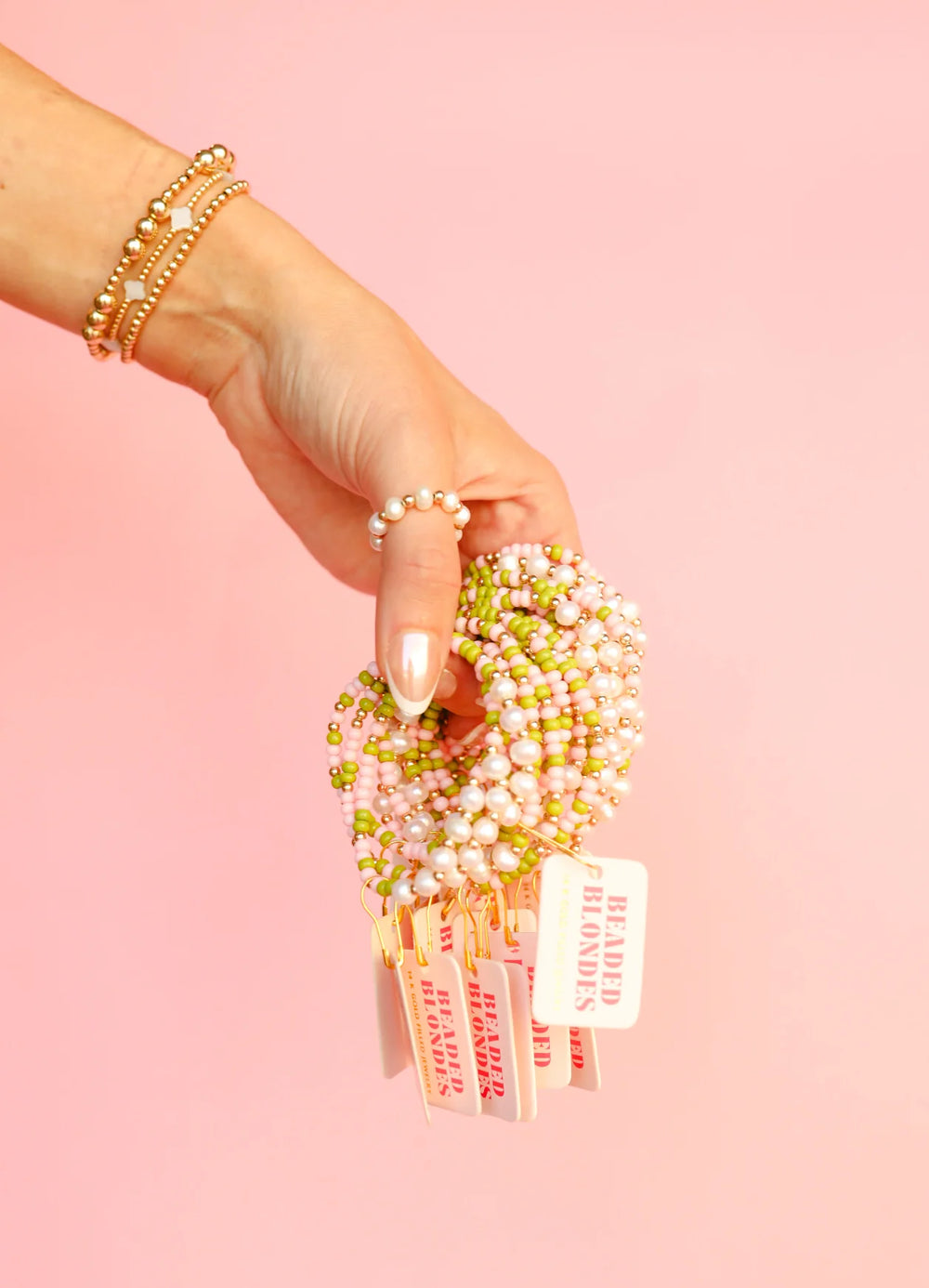 Person holding a set of beaded blonde bracelets with a pink background