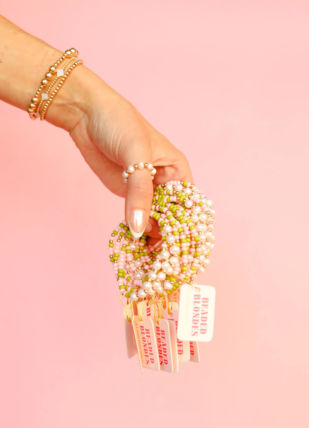 Person holding a set of beaded blonde bracelets with a pink background