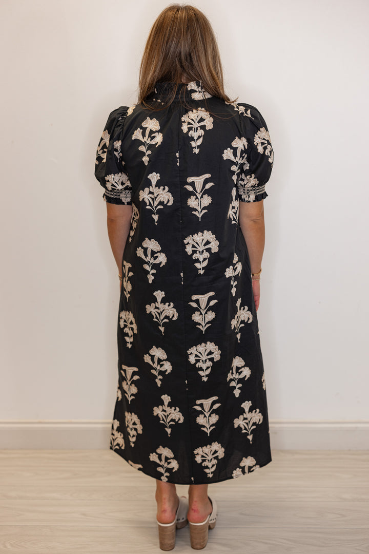 back view of Women's black midi dress with taupe botanical floral print and ruffle detail