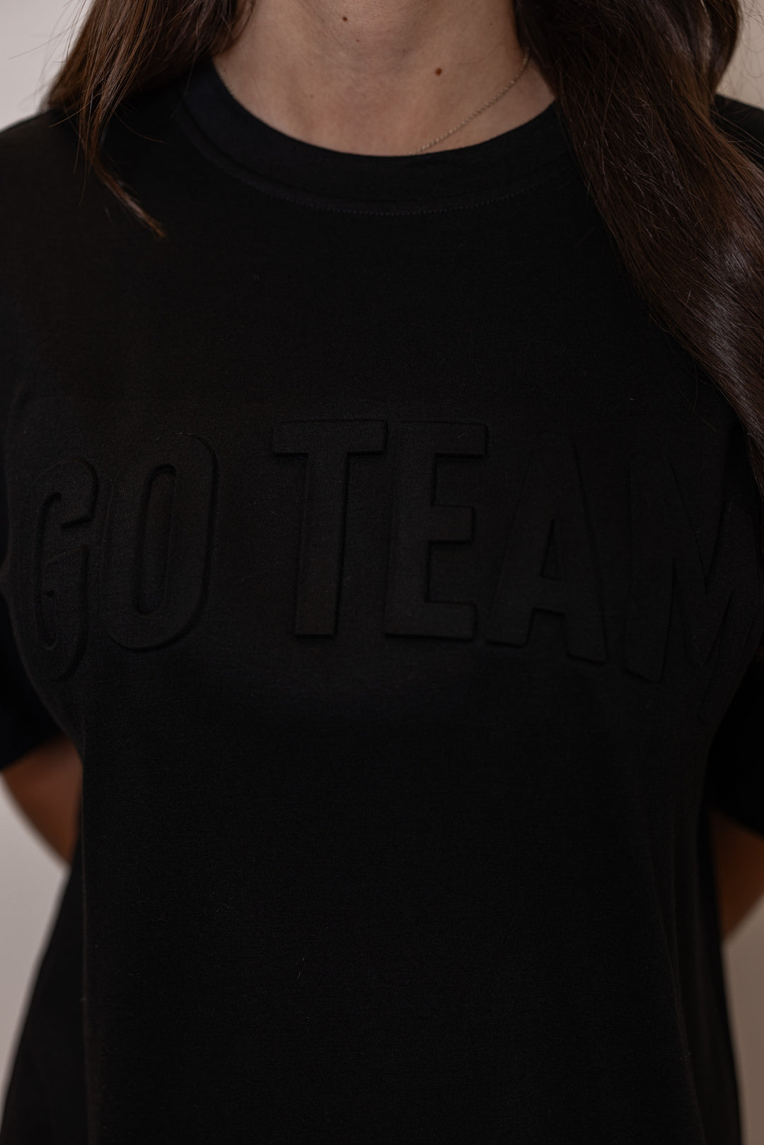 Women's black lightweight top with embossed 'Go Team' in center by Jess Lea, showing up close view of embossed lettering