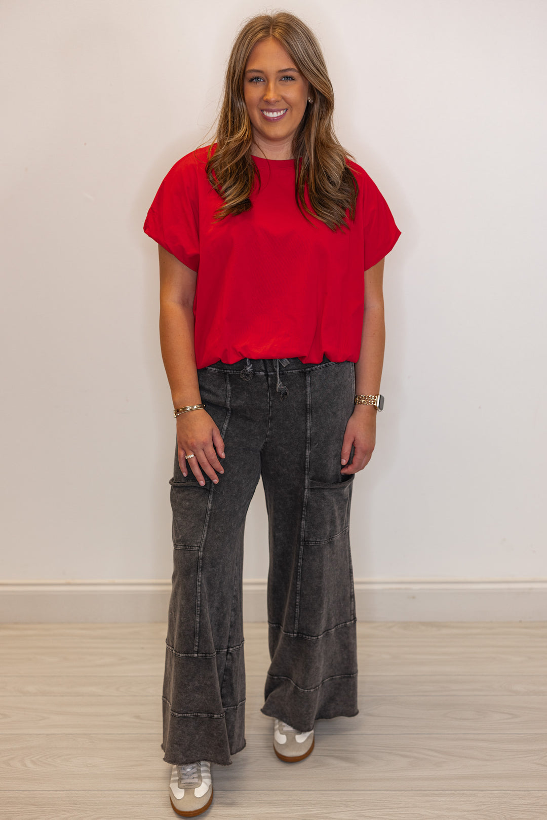 Woman wearing a red top and dark jeans against a plain background