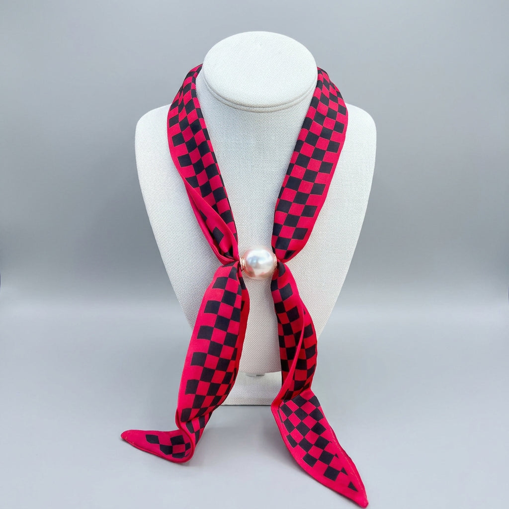 A red and black checkered silk scarf  featuring a central white pearl bead with magnetic closure