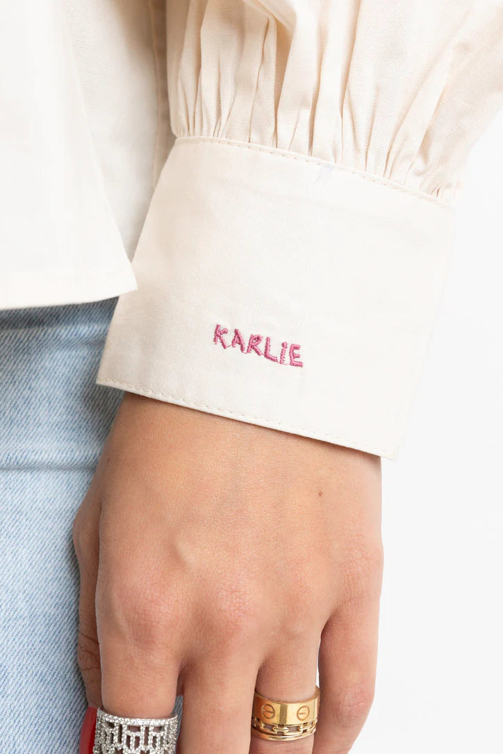 Women's ivory button front top with ruffle trim details by Karlie showing emblem on cuff