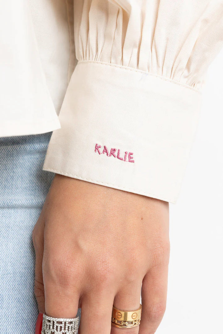 Women's ivory button front top with ruffle trim details by Karlie showing emblem on cuff