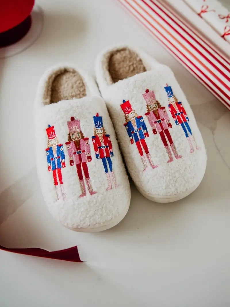 Pair of white slippers with nutcracker design on a light surface.
