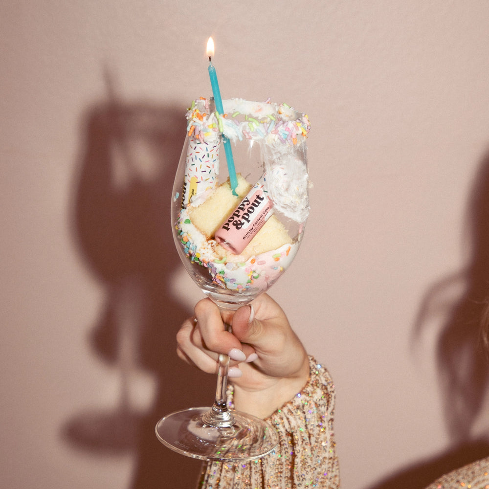 Wine glass filled with cake, candles, and sprinkles and poppy and pout lip balm
