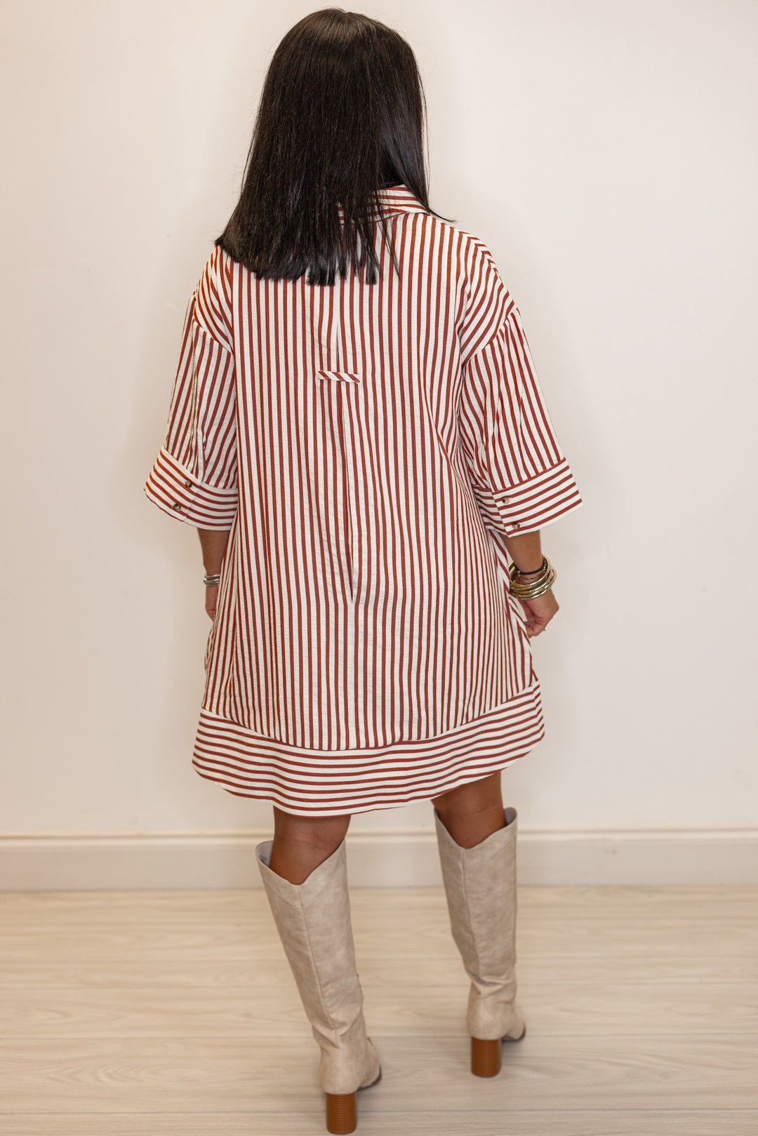 back view of Woman's rust and ivory striped dress with beige knee-high boots 