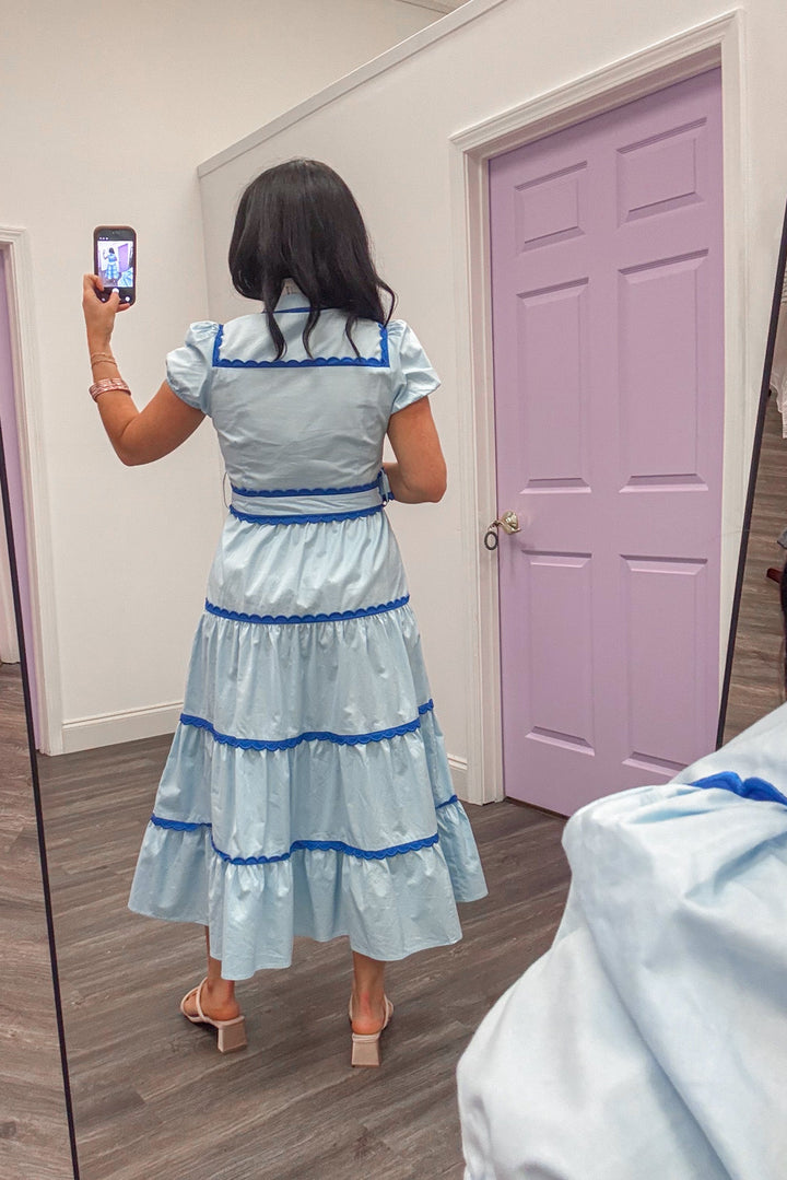 Women's light blue tiered midi dress with dark blue scalloped piping trim showing full back view